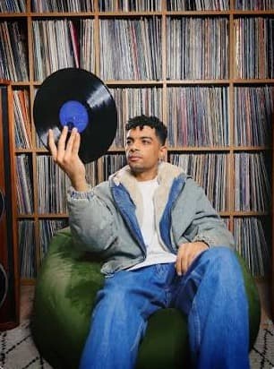 Kirollus holding a record in front of shelves of vinyl